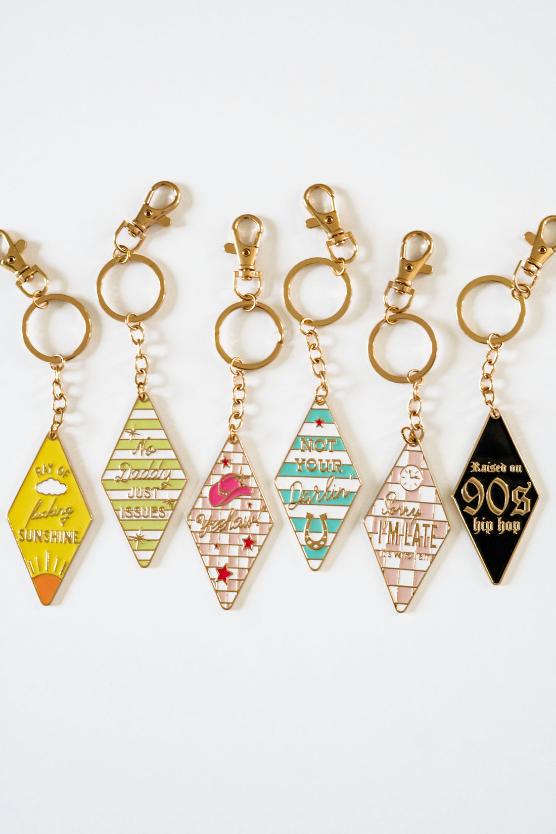 Retro motel keychain collection featuring vintage motel key tag style enamel keychains with gold hardware, colorful stripes, and playful sayings