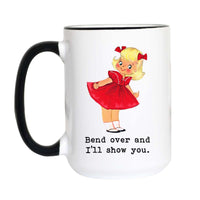 A white ceramic mug with a black handle and black rim, featuring a cartoon illustration of a blonde girl in a red dress and the text 'Bend over and I'll show you.' on a white background.
