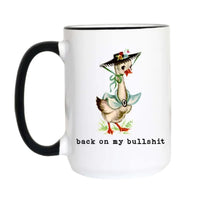 A white ceramic mug with a black handle and black rim, featuring a vintage-style illustration of a goose wearing a sombrero and bow tie, with the text 'back on my bullshit' printed below.