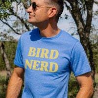 A person wearing a blue t-shirt with the text 'BIRD NERD' printed on the front is using binoculars outdoors.