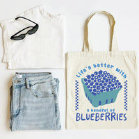 White t-shirt, blue jeans, sunglasses, and a tote bag with blueberries design on a white background