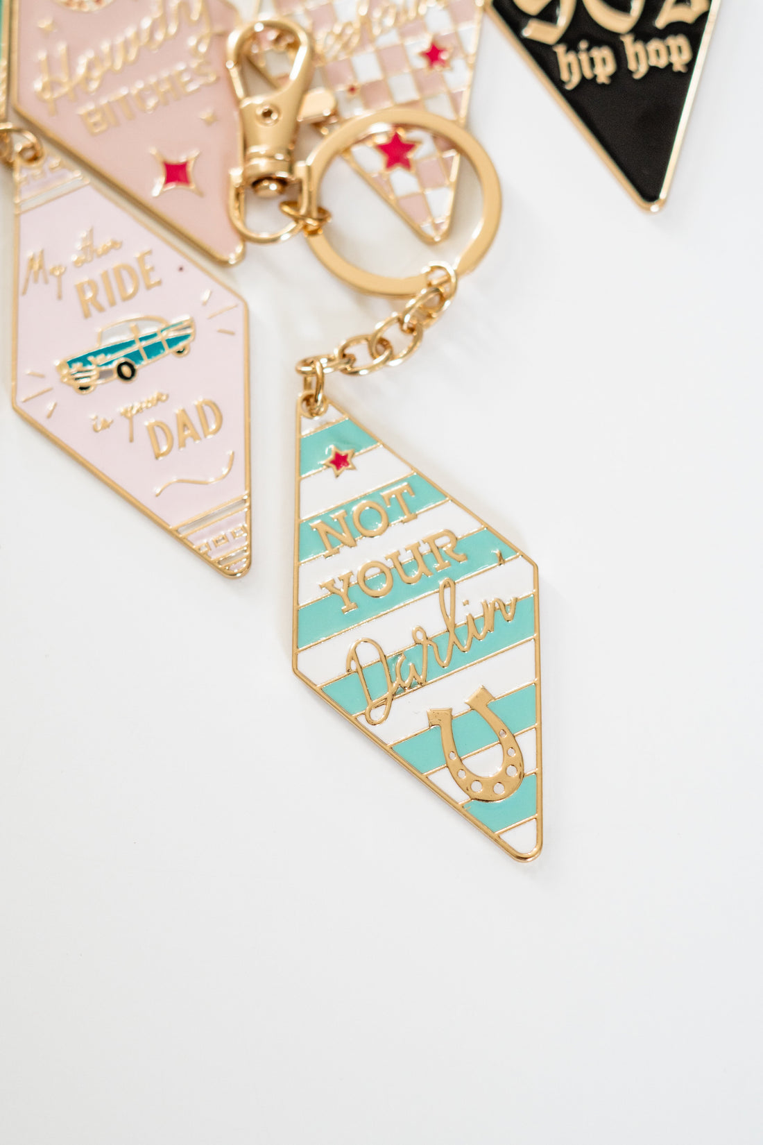 Vintage-style motel keychains reading "Not Your Darlin" and "My Other Ride is My Dad", pastel enamel tags with gold ring and retro design