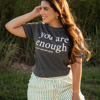 Woman wearing a t-shirt with 'you are enough' text, standing outdoors.