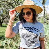 Person wearing a 'MEOWDY' t-shirt with a cat graphic outdoors.