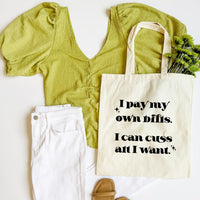 Green top, white pants, beige sandals, and a tote bag with text on a white background