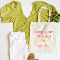 Green top, white pants, beige tote bag with text, and green plant on a white background