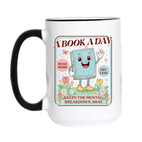 A white ceramic coffee mug with a black handle and black rim, featuring a colorful cartoon graphic of a book character with the text 'A BOOK A DAY KEEPS THE MENTAL BREAKDOWN AWAY'.