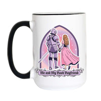 A white ceramic mug with a black handle and black rim, featuring a graphic of a knight in armor and a woman in a pink dress under a purple arch, with the text 'Me and My Book Boyfriend' below.
