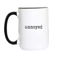 Funny mood coffee mug with black typewriter text reading "annoyed" on a white mug with black accent handle and rim
