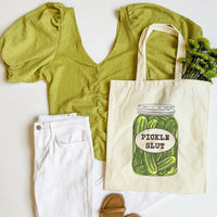 Green top, white pants, and tote bag with pickle design on a white background