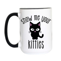 A white ceramic mug with a black handle and black rim, featuring a black cartoon cat graphic with pink inner ears and the text 'show me your kitties' in black script.