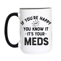 A white ceramic coffee mug with a black handle and black interior rim, featuring the printed text 'IF YOU'RE HAPPY AND YOU KNOW IT IT'S YOUR MEDS' in black lettering on the front.