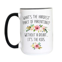 A white ceramic mug with a black handle and black rim, featuring the humorous quote 'WHAT'S THE HARDEST PART OF PARENTING? WITHOUT A DOUBT.