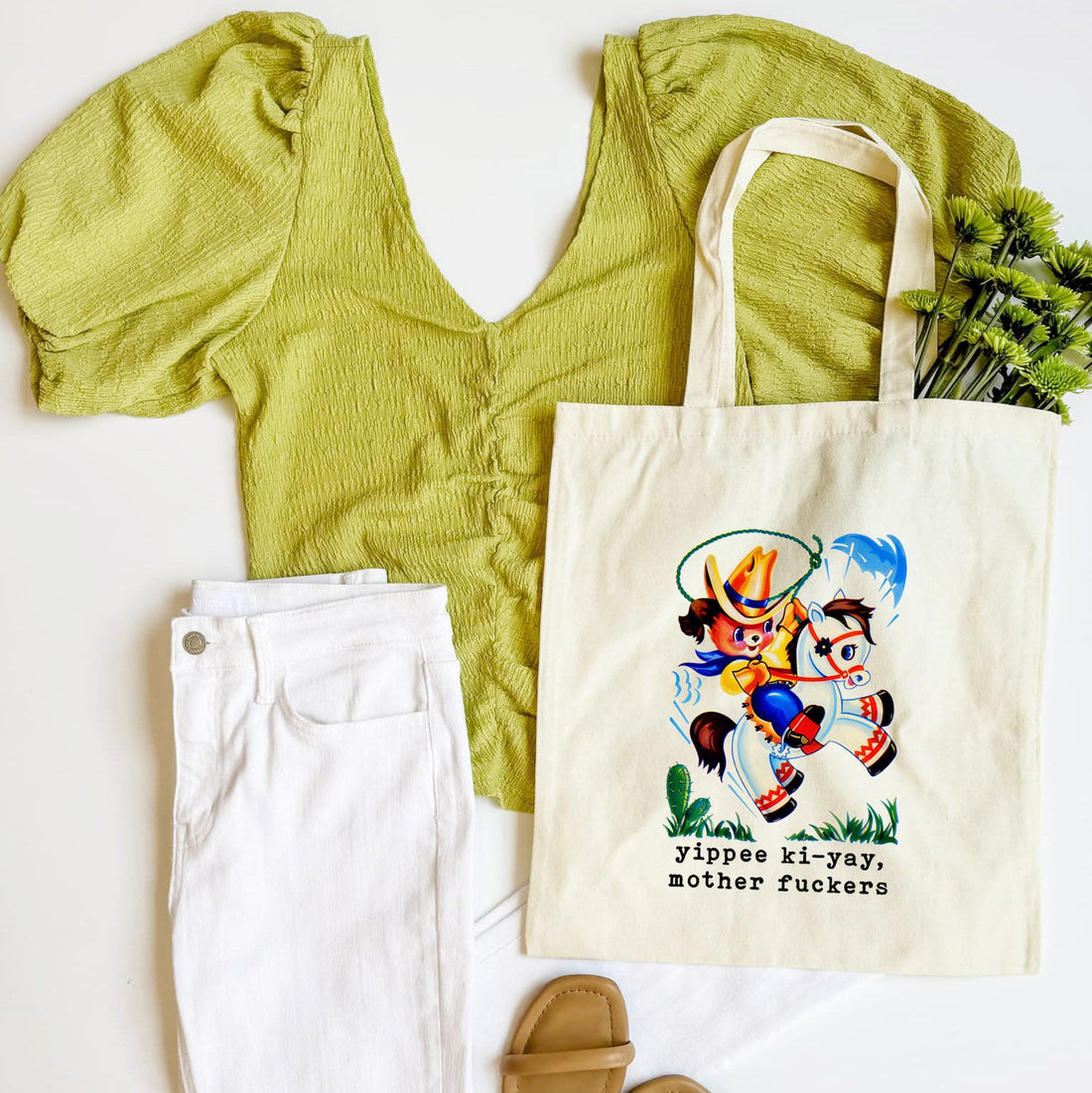 Green top, white pants, beige sandals, and a tote bag with a graphic design on a white background