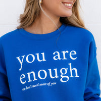 Person wearing a blue sweatshirt with 'you are enough' text on a plain background