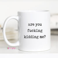 White mug with text 'are you fucking kidding me?' on a blurred background