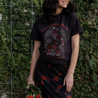 Person wearing a black t-shirt with a graphic design against a green wall.