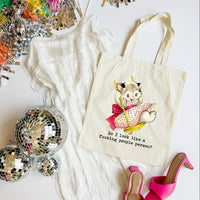Tote bag with a cat illustration and text, surrounded by disco balls and high heels on a white surface.