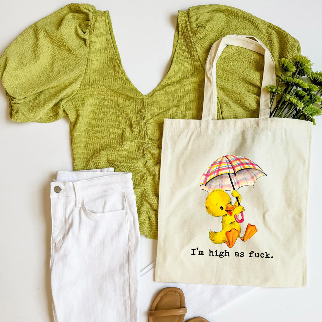 Green top, white pants, brown sandals, and a tote bag with a duck graphic on a white background
