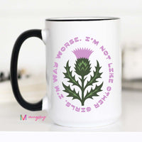 White mug with green thistle design and pink text on a white background