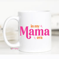 White mug with 'in my Mama era' text in pink and orange on a white background