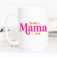 White mug with 'in my Mama era' text in pink and orange on a white background