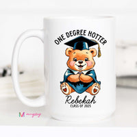 A white ceramic coffee mug with a black handle featuring a cartoon bear wearing a graduation cap and the text 'One Degree Hotter', with a personalized name 'Rebekah' and 'Class of 2021'.