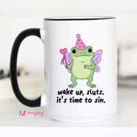 Mug with a cartoon frog wearing a party hat and fairy wings, with text 'wake up, sluts. it's time to sin.'