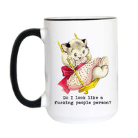 A white ceramic coffee mug with a black handle and black rim, featuring a retro illustration of a kitten on a swing with the text 'Do I look like a fucking people person?' printed below.