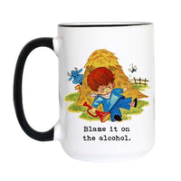 A white ceramic mug with a black handle and black rim, featuring a cartoon illustration of a boy in a blue suit blowing a red horn in front of a hay bale, with the text 'Blame it on the alcohol.' printed below.