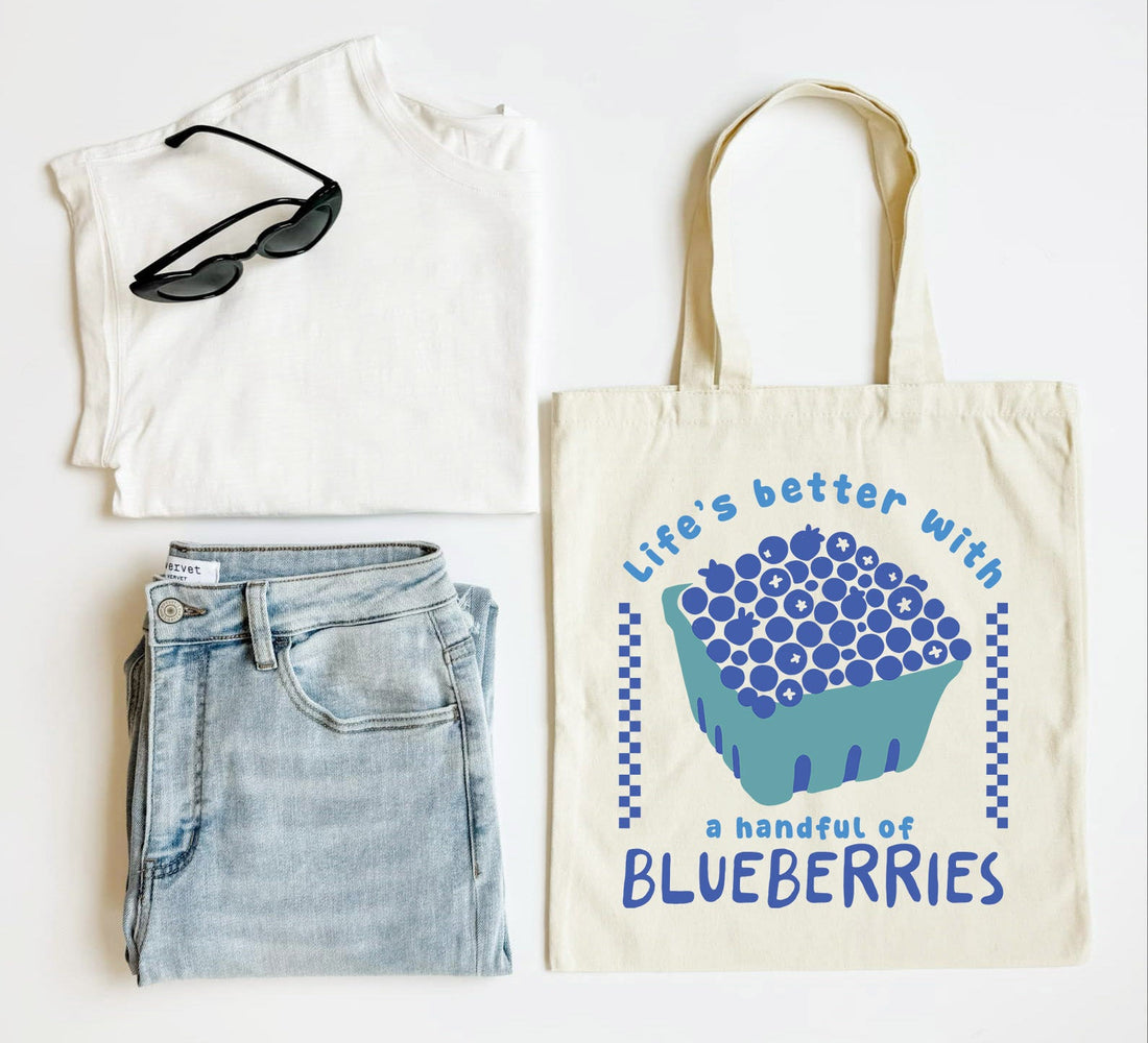 White t-shirt, blue jeans, sunglasses, and a tote bag with blueberries design on a white background