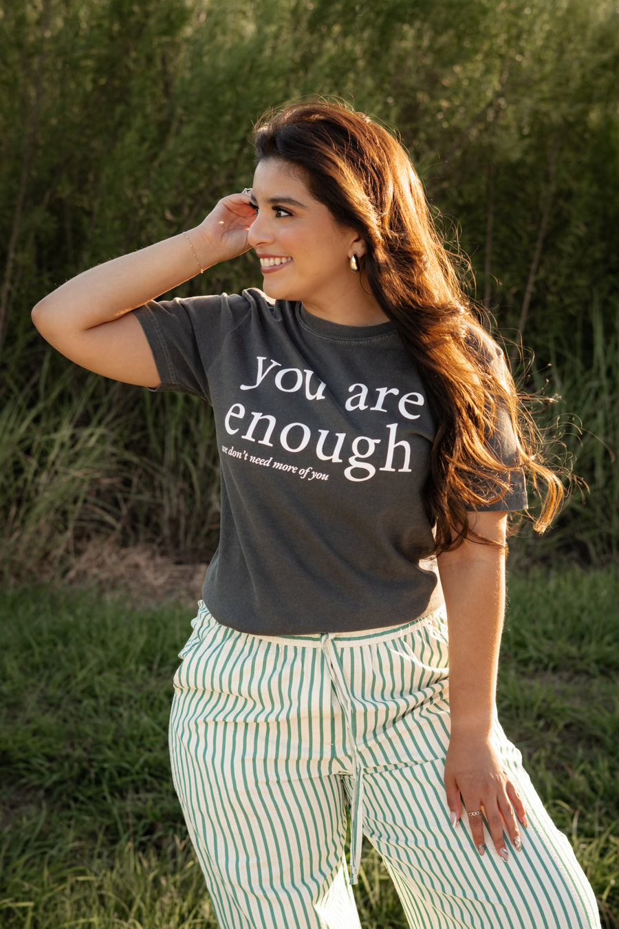 Woman wearing a t-shirt with 'you are enough' text, standing outdoors.