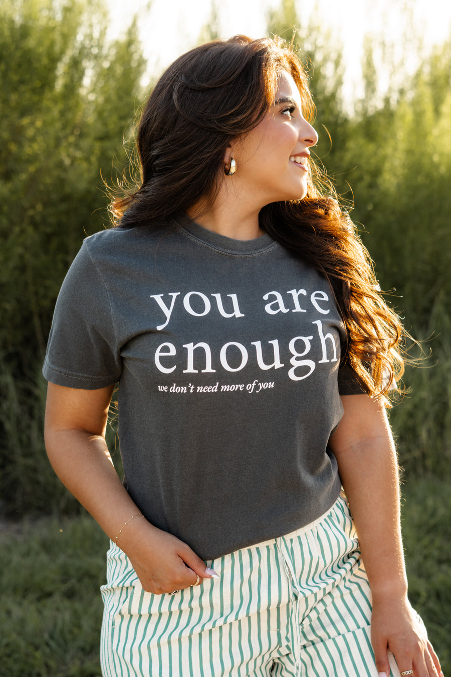 Woman wearing a t-shirt with 'you are enough' text in a natural setting
