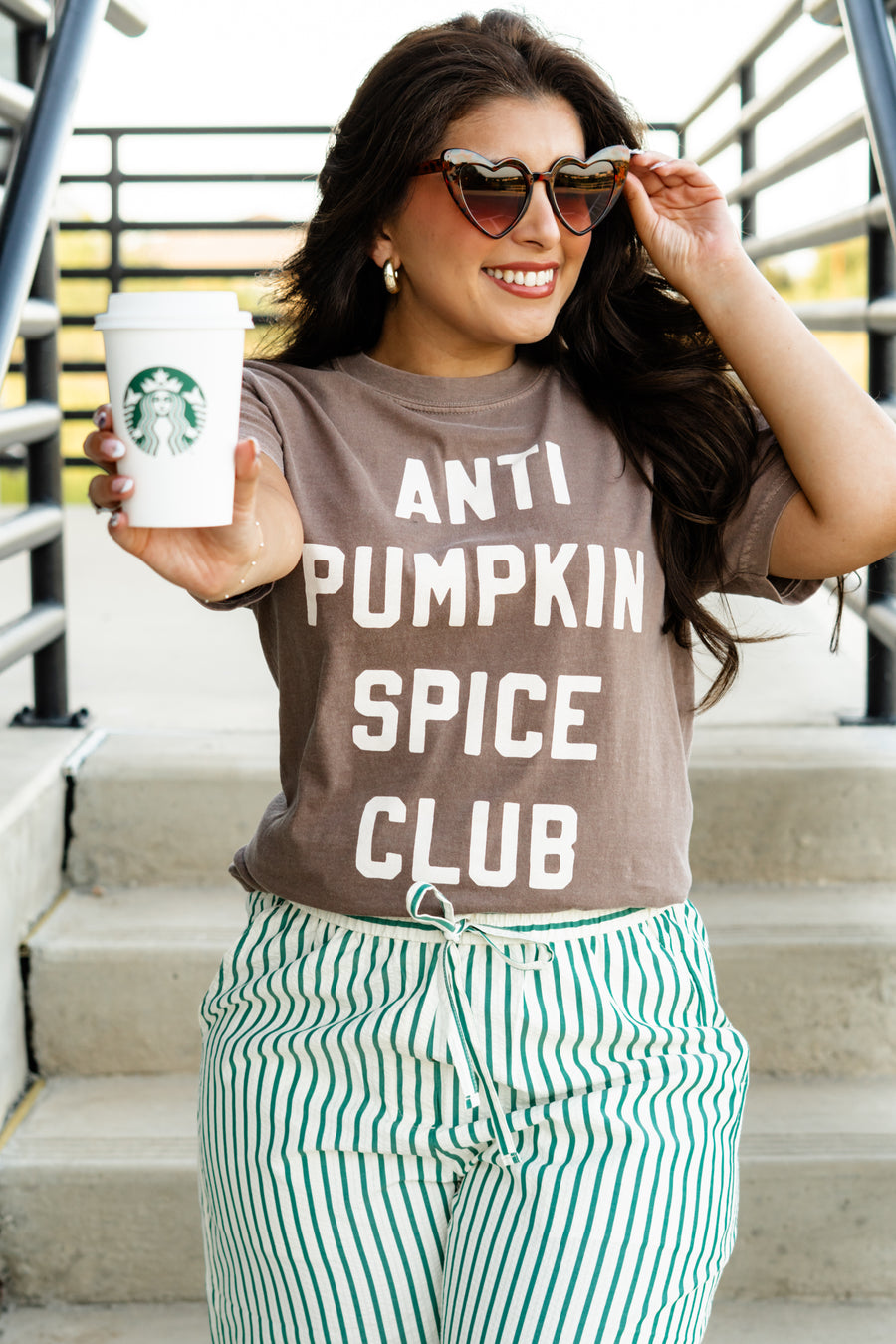 Woman wearing an 'ANTI PUMPKIN SPICE CLUB' t-shirt, holding a Starbucks cup.