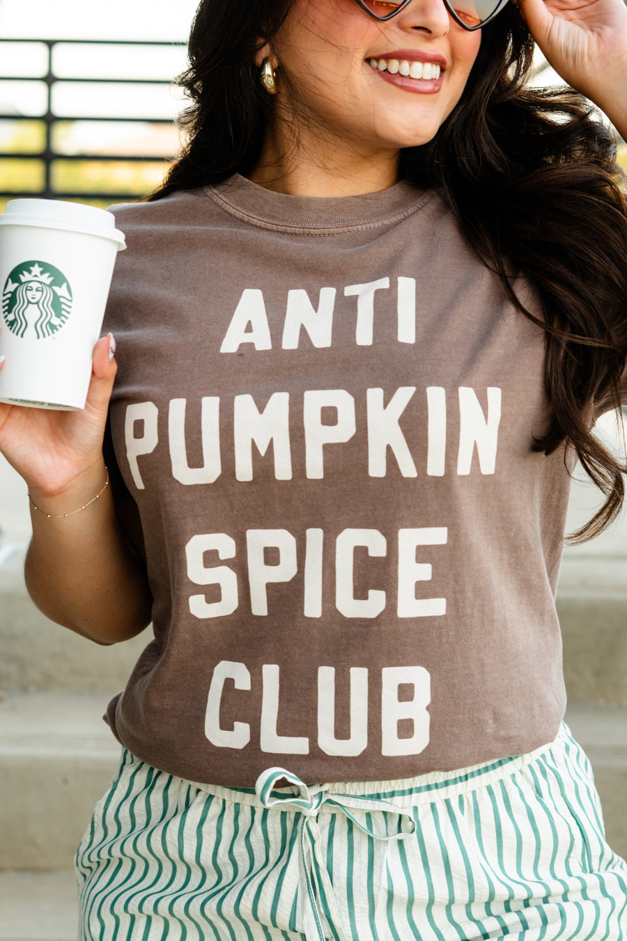 Person wearing a 'ANTI PUMPKIN SPICE CLUB' shirt holding a Starbucks cup.