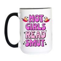 A white ceramic coffee mug with a black handle and black rim, featuring a pink and purple graphic that reads 'HOT GIRLS READ SMUT' with flame and star accents.