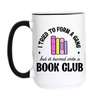 A white ceramic mug with a black handle and black rim, featuring a graphic design that reads 'I TRIED TO FORM A GANG but it turned into a BOOK CLUB' with colorful book illustrations.