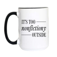 A white ceramic coffee mug with a black handle and black interior rim, featuring the printed text 'IT'S TOO nonfictiony OUTSIDE' in black lettering on the front.