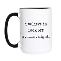 Funny introvert coffee mug with black typewriter text reading "i believe in fuck off at first sight." on a white mug with black accent handle and rim

