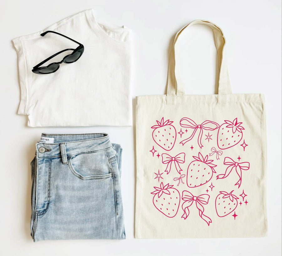 White t-shirt, blue jeans, black sunglasses, and a tote bag with strawberry and bow pattern on a white background