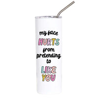 A white insulated tumbler with a clear lid and metal straw, printed with the humorous phrase 'my face HURTS from pretending to LIKE YOU' in black and pastel colors, on a solid white background.