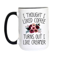 A white ceramic coffee mug with a black handle and black rim, featuring the printed text 'I THOUGHT I LIKED COFFEE TURNS OUT I LIKE CREAMER' in black lettering around a floral graphic of pink, burgundy, and green flowers.