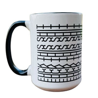 A white ceramic mug with a black handle and black geometric tribal-style patterns printed on the side, shown against a plain white background.