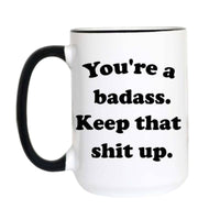 A white ceramic mug with a black handle and black rim, featuring the printed text 'You're a badass. Keep that shit up.