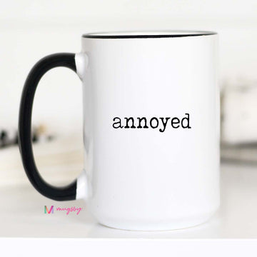 White mug with black handle and 'annoyed' text on a white background
