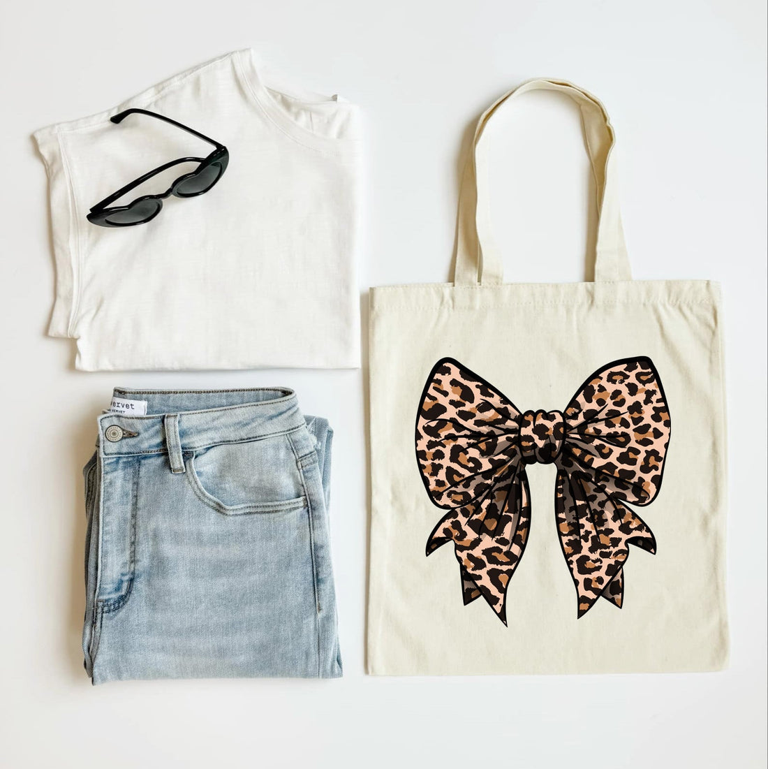 White sleeveless shirt, blue jeans, black sunglasses, and a tote bag with a leopard print bow on a white background.
