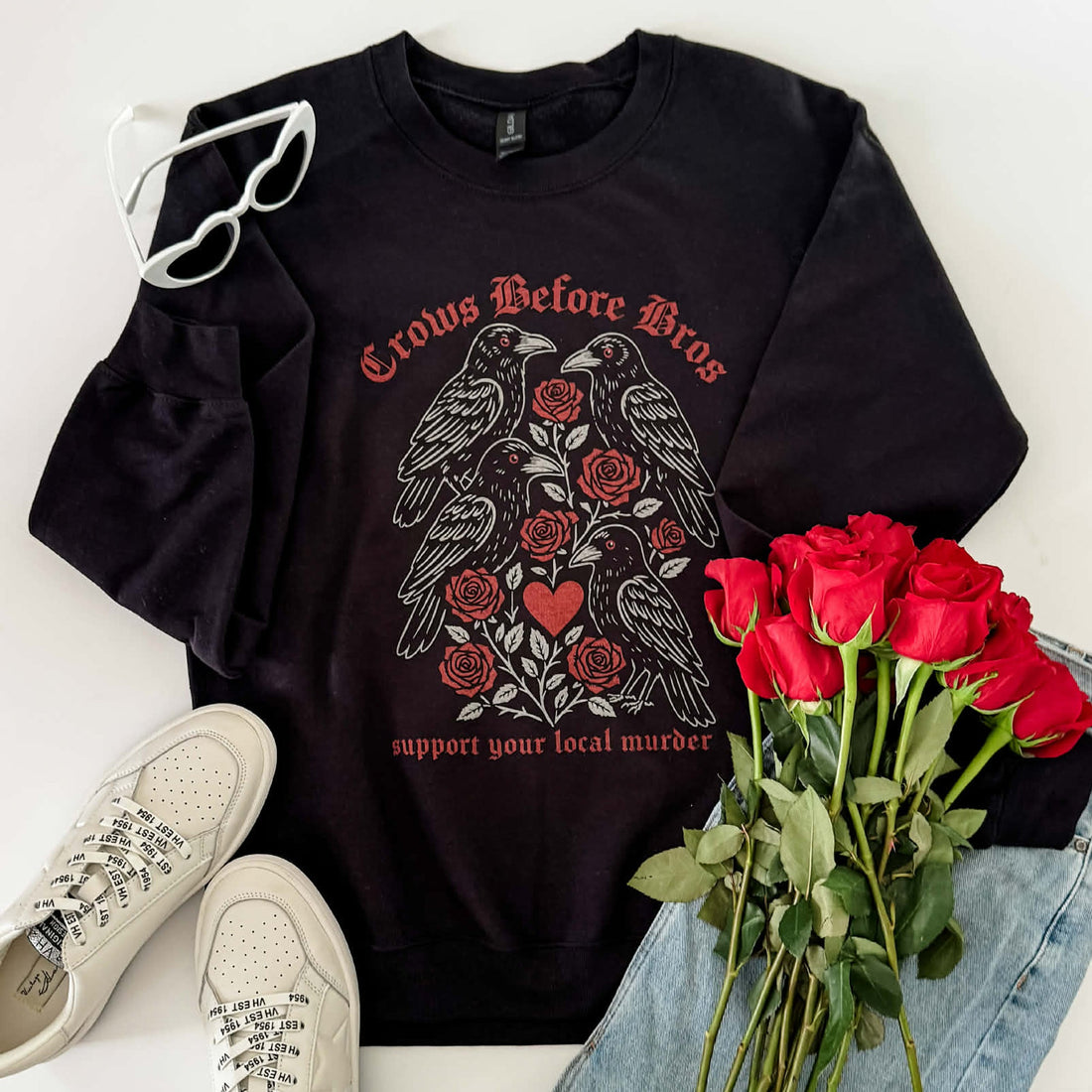 Black sweatshirt with crow and rose design, white sneakers, red roses, and denim jacket on a white background