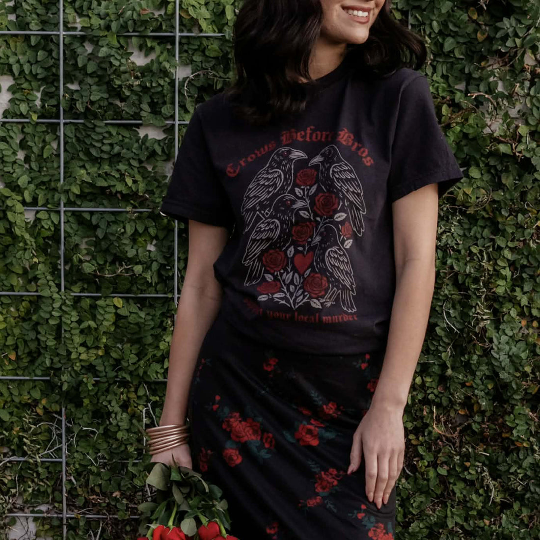 Person wearing a black t-shirt with a graphic design against a green wall.