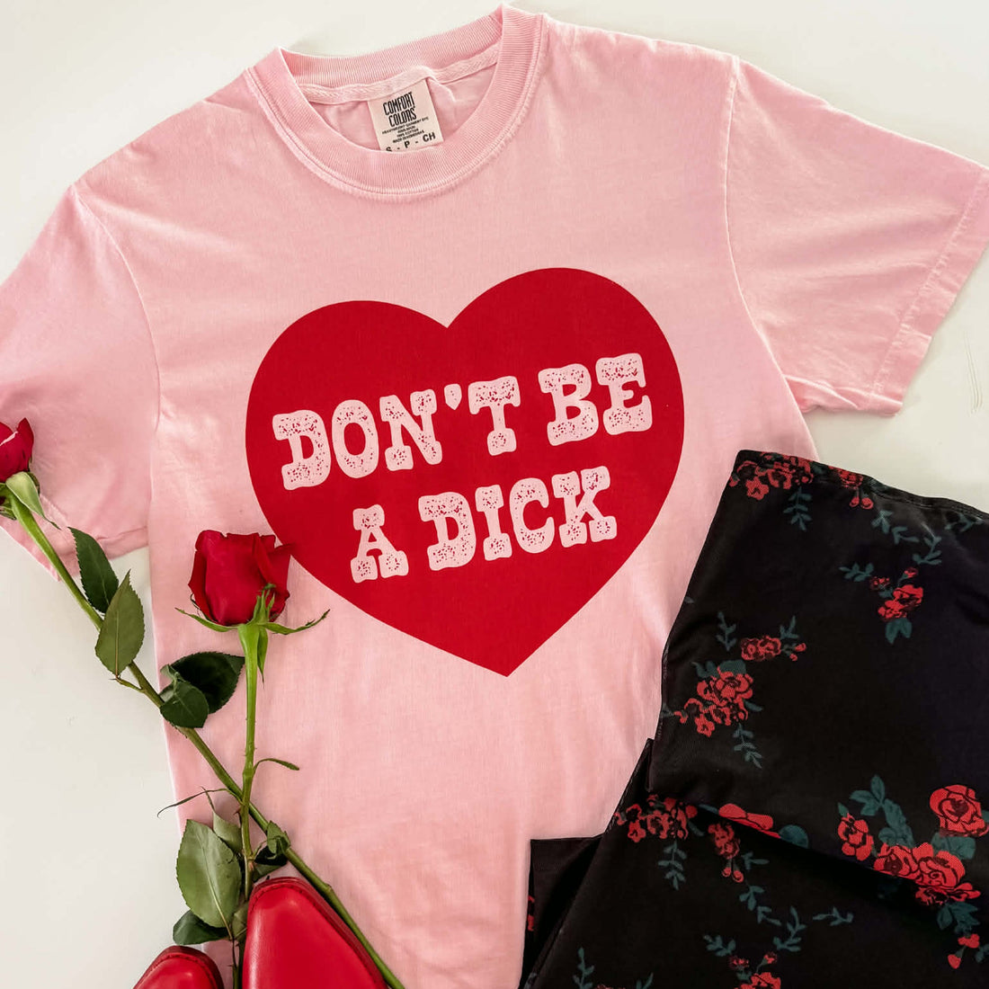 Pink t-shirt with a red heart and text, next to a rose and black floral dress.