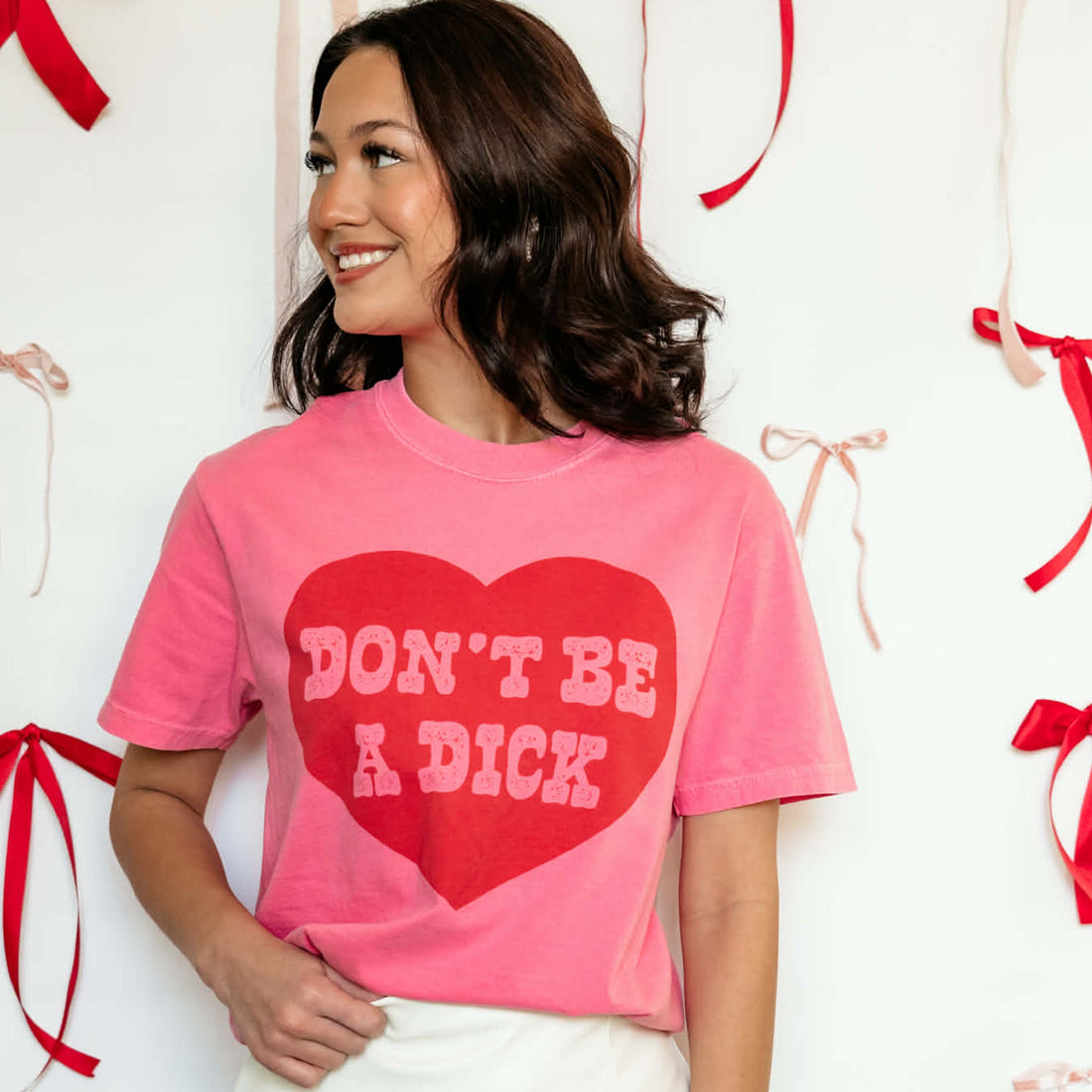 Woman wearing a pink t-shirt with a red heart and text, surrounded by decorative ribbons.